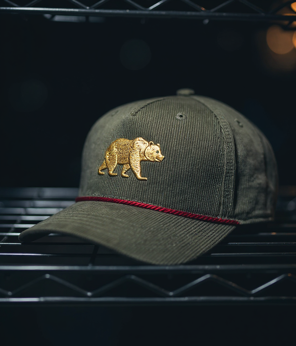 Olive corduroy cap with a gold bear embroidered on the front — stitched on our press floor